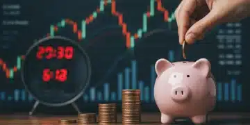 Hand putting coins into piggy bank with financial charts in background